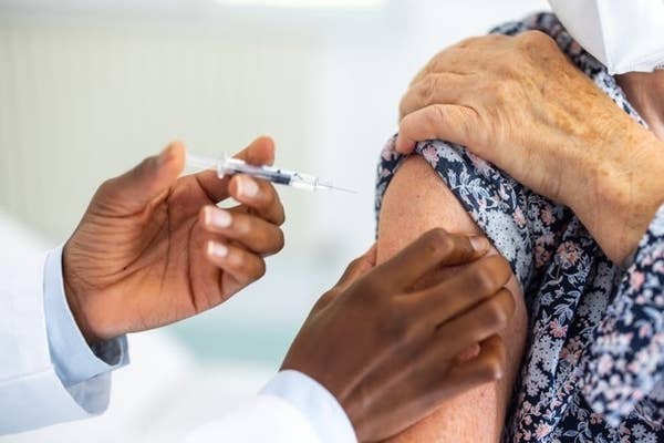 Person receiving a vaccine injection in the upper arm, administered by a healthcare professional