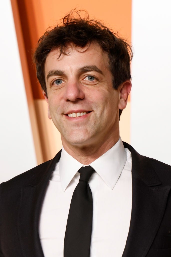 Person in a formal suit and tie smiles at the camera against a geometric background