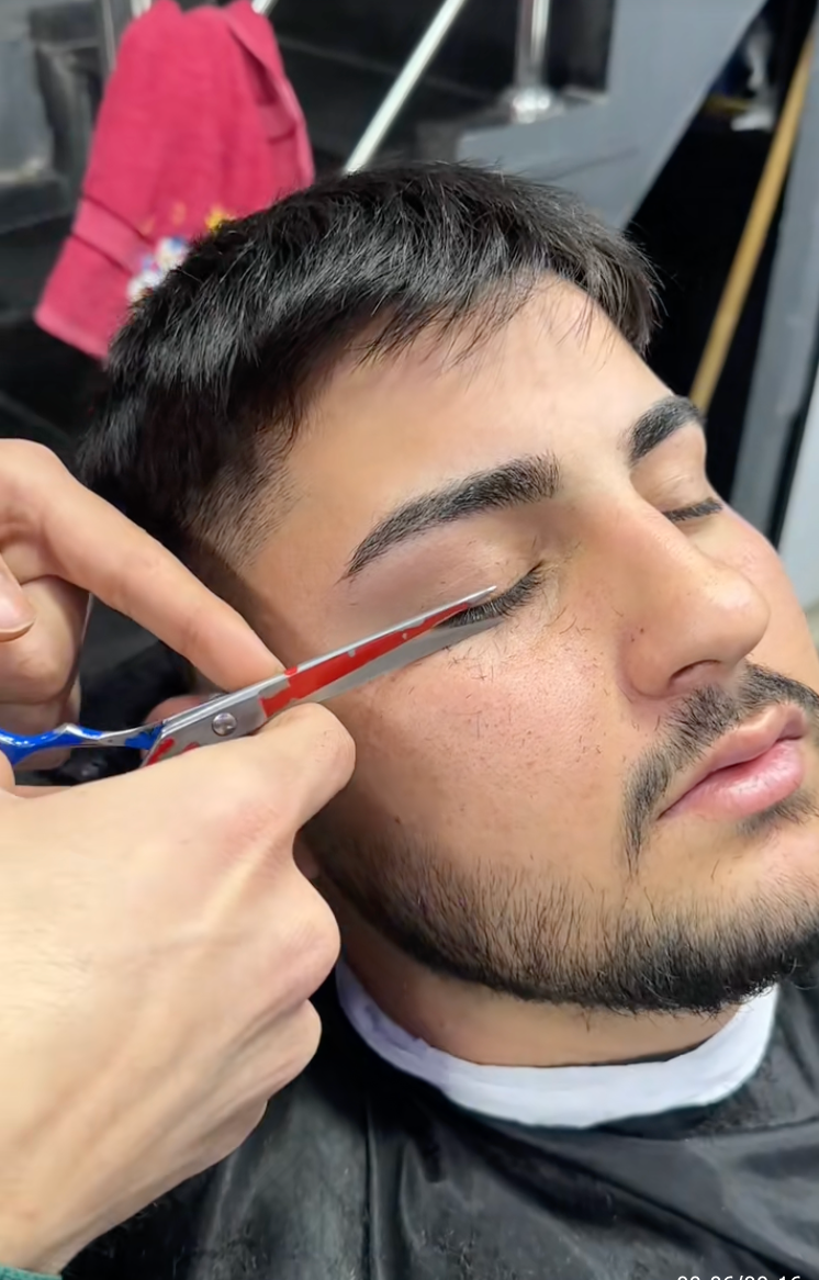 Person getting eyebrows trimmed with scissors at a salon, eyes closed, relaxed