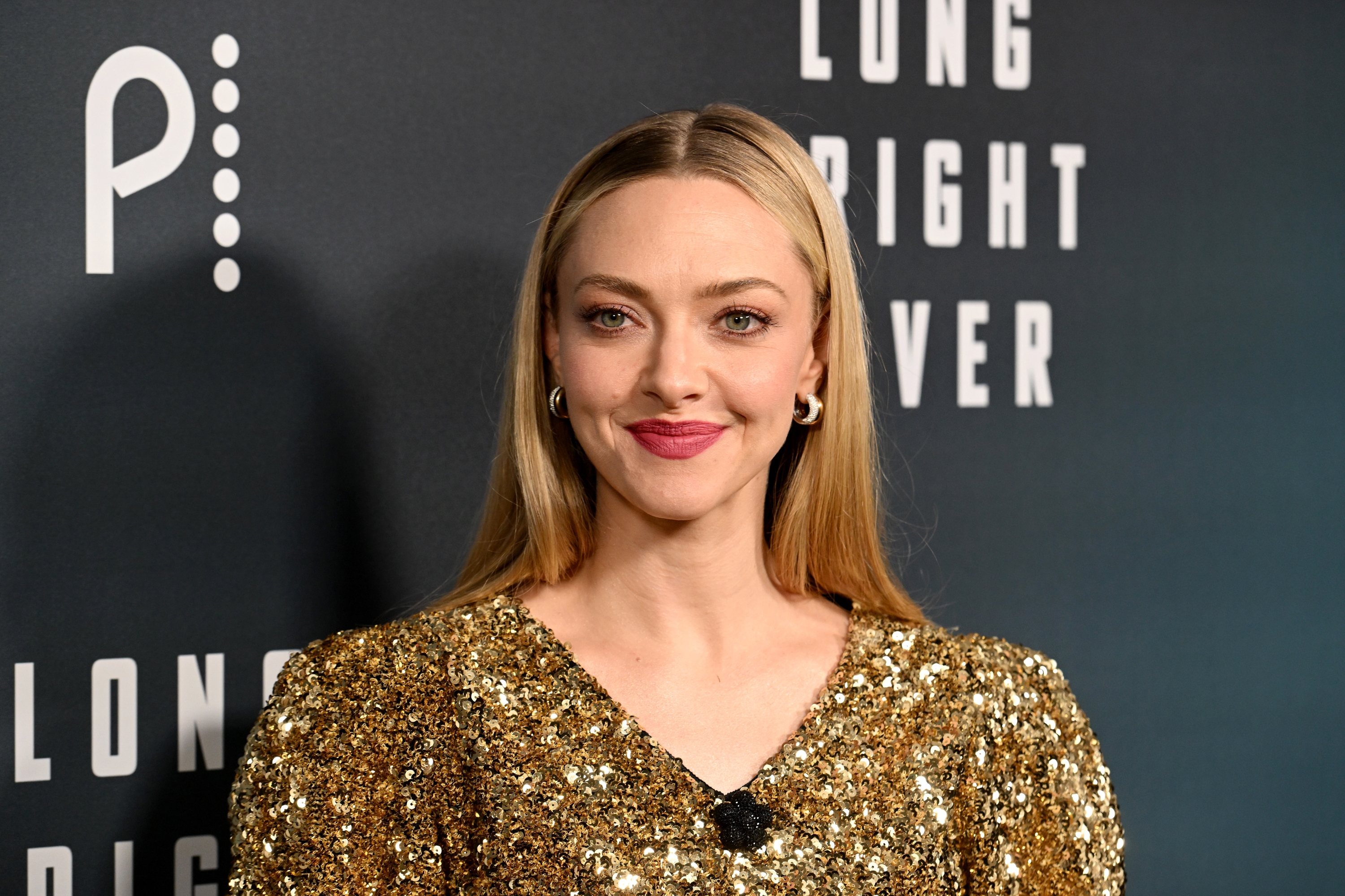 Amanda Seyfried in sparkling dress with structured shoulders smiles at a media event
