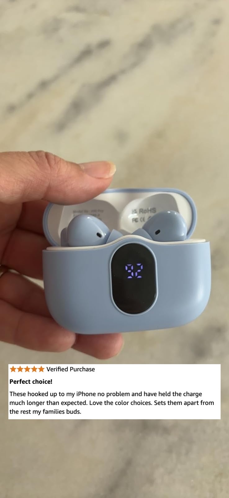 A hand holds a pair of wireless earbuds in an open charging case with a digital display showing the battery level