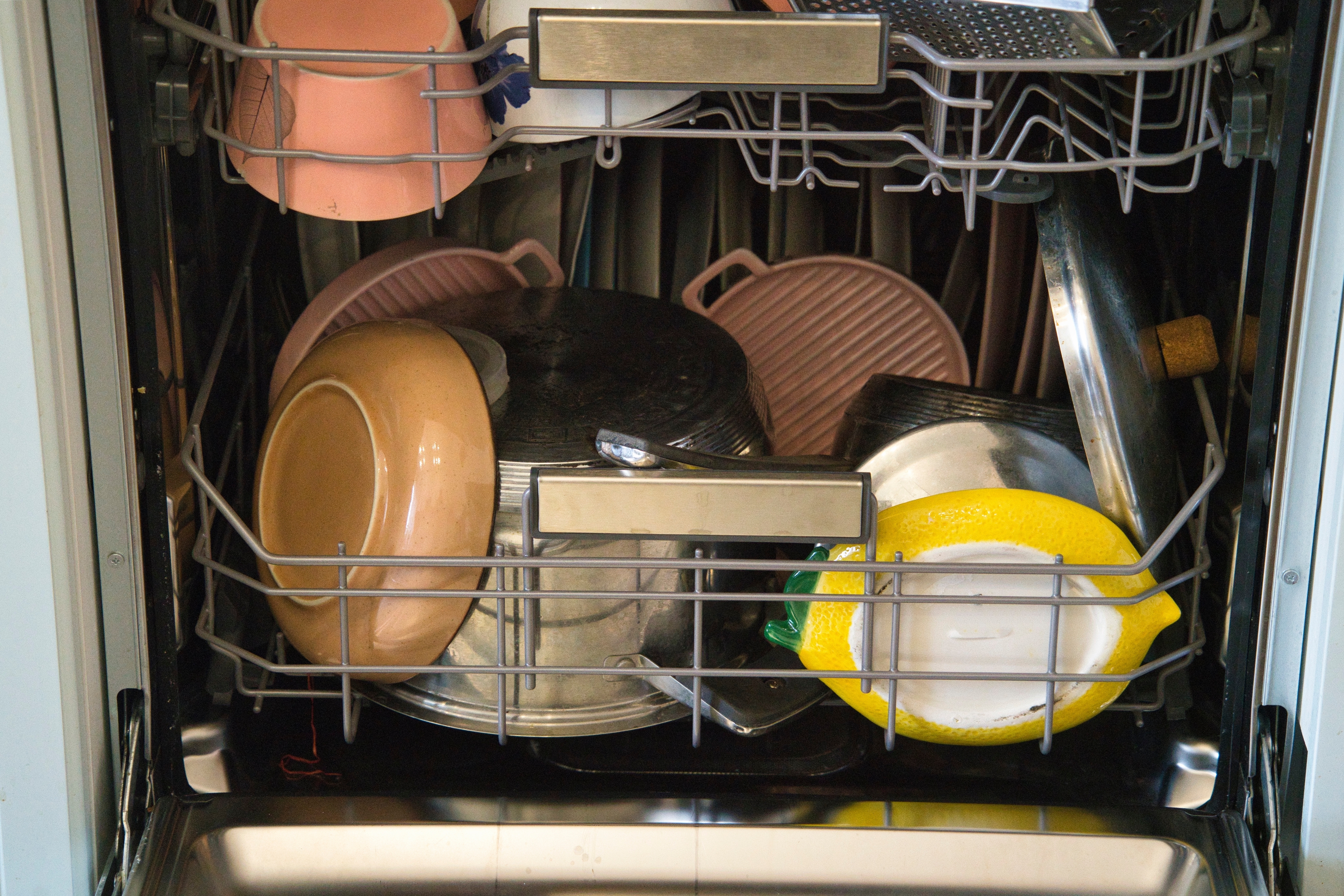 Open dishwasher filled with various dishes, including plates, pots, and a plastic lemon-shaped container