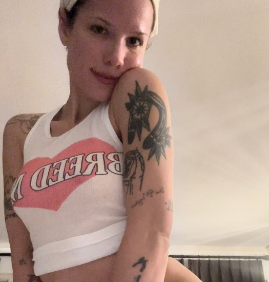 halsey posing indoors, wearing a sleeveless top with visible tattoos on arms, including a star design