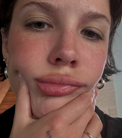 halsey with short hair looks directly at the camera, gently pinching their face with one hand. Wearing hoop earrings and a ring