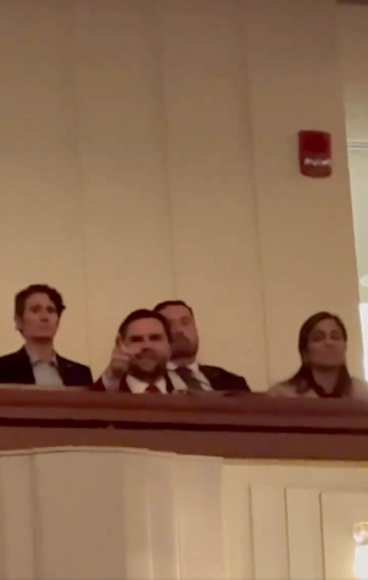 Group of people in balcony seats at an event, one person pointing