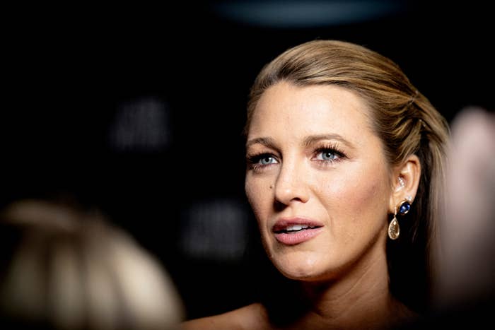Blake Lively on the red carpet with elegant hairstyle, wearing drop earrings and strapless attire, looking attentively to the side