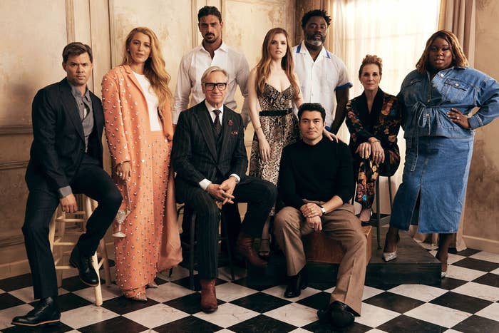 The cast of Another Simple Favor in formal and unique attire posing stylishly indoors on a checkered floor with some sitting and others standing