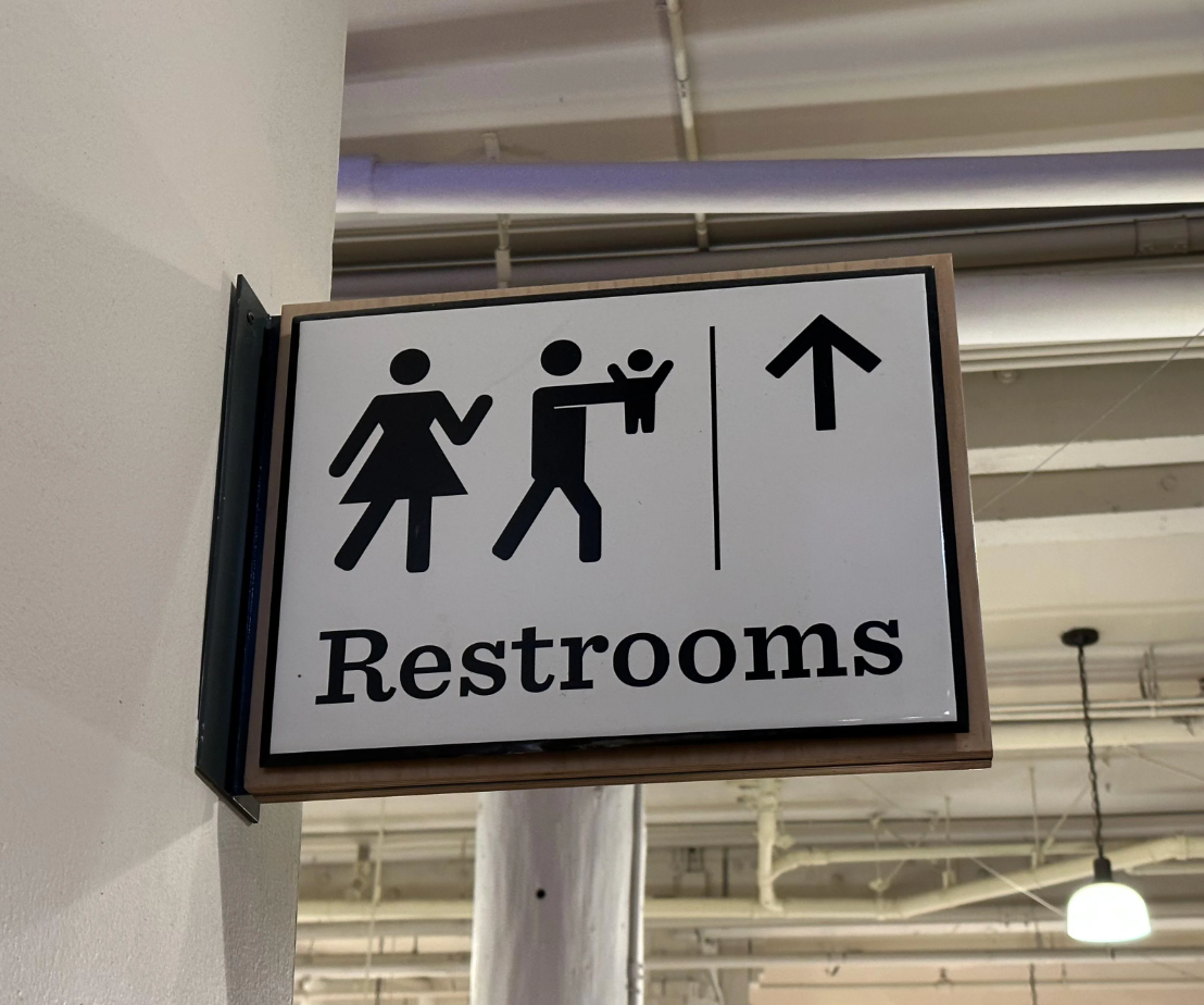 Restroom sign with icons for men, women, and accessible/family facilities. Arrow points upward for direction