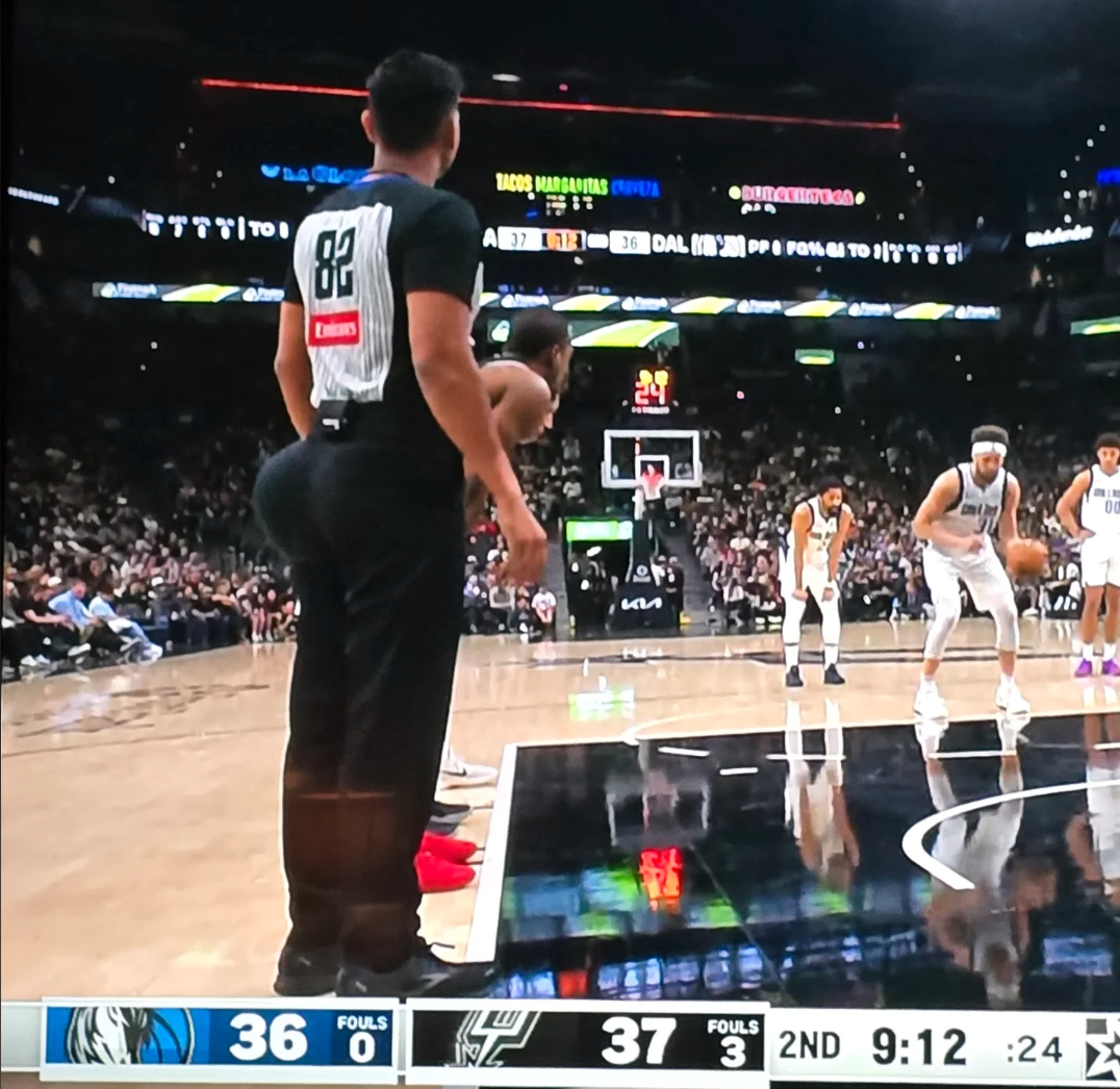 Basketball game in progress with a player preparing to shoot a free throw. Another player stands near the sideline. Scoreboard shows Dallas 36, Spurs 37