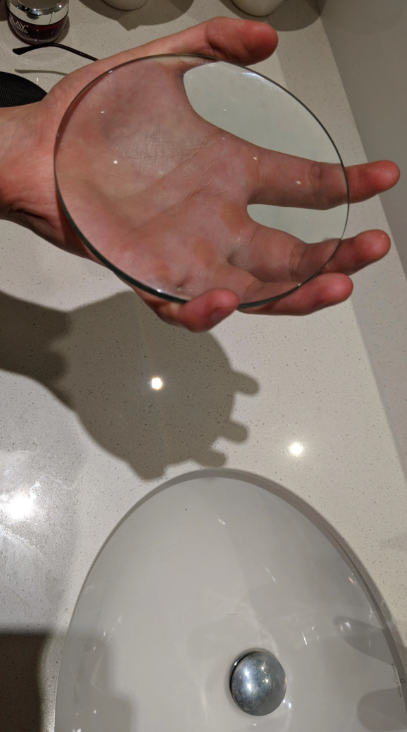 Hand holding a round glass disc over a bathroom sink, casting a shadow on the countertop