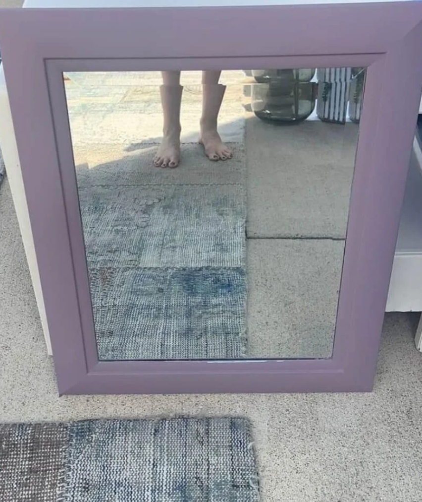 A mirror on the floor reflects a person&#x27;s bare feet and part of their legs, set against a room with various textured rugs