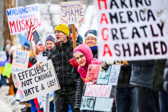 Protesters hold various signs, including &quot;Efficiency... Not Carnage, Hate &amp;amp; Lies&quot; and &quot;Making America Greatly Shamed,&quot; expressing political dissent