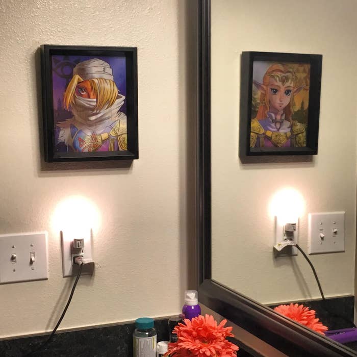 Two framed portraits of fantasy characters are displayed above a bathroom counter with a mirror and toiletries