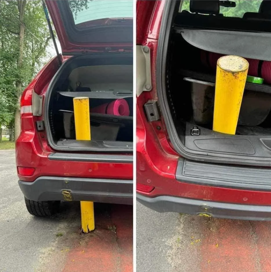 A car is parked over a yellow pole, unable to drive away, with the pole stuck under the rear bumper