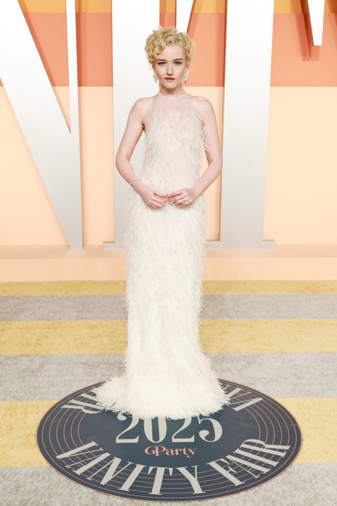 Person in a glamorous feathered gown poses at a Vanity Fair event