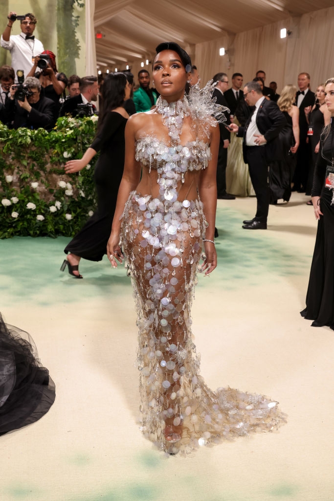 Person in shimmering, intricate gown with translucent elements on a red carpet at a formal event, posing while photographers capture the moment