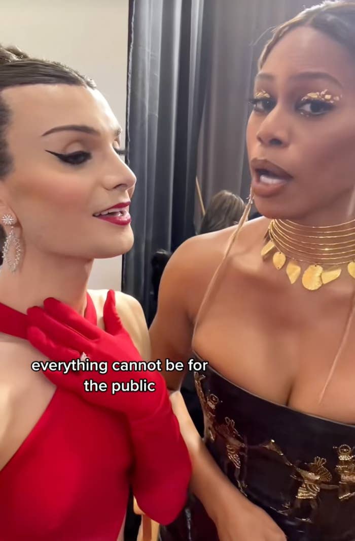 Laverne Cox wearing a gold choker and strapless dress while talking to Dylan Mulvaney at the Grammys