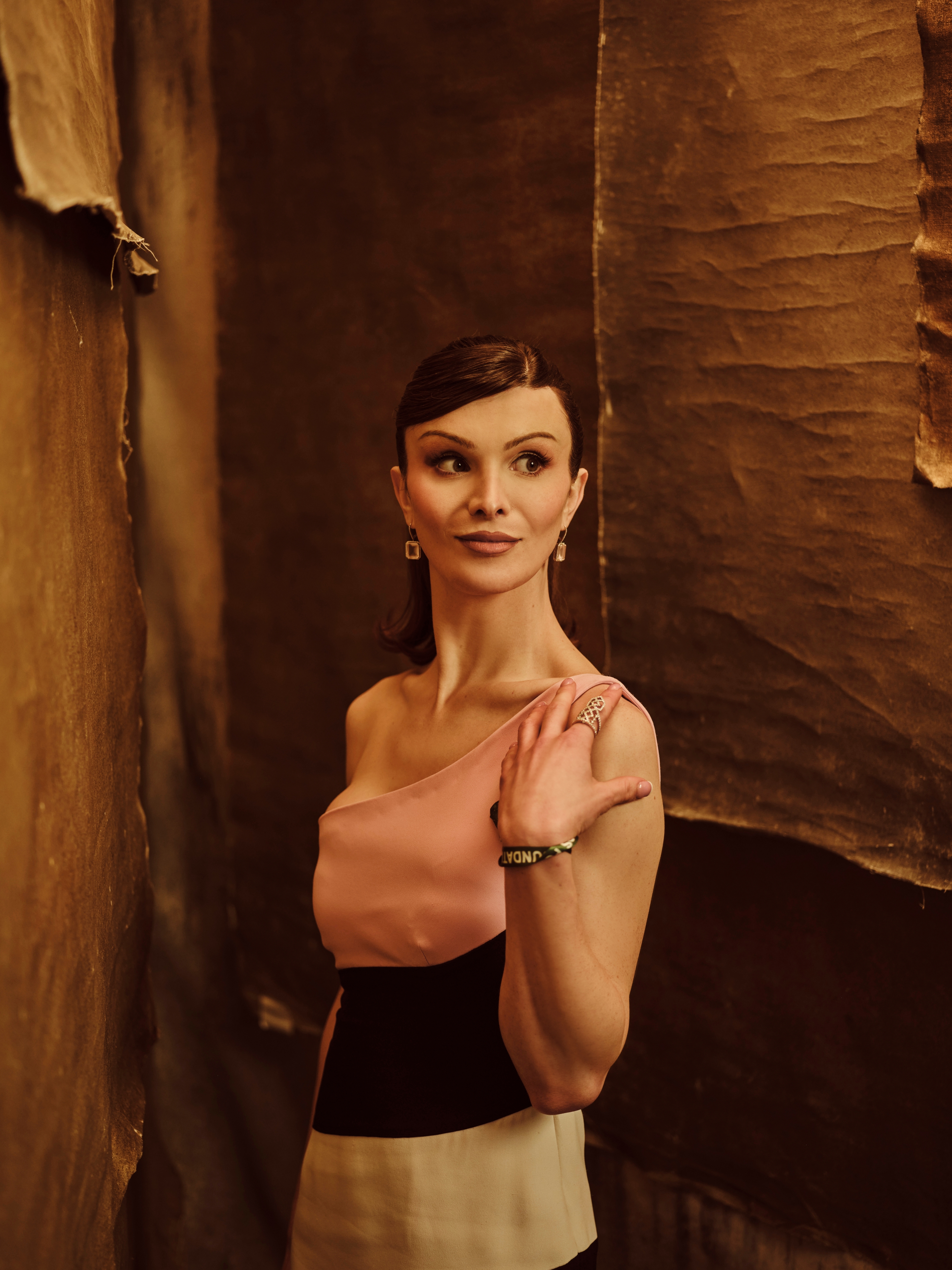 Dylan Mulvaney in an elegant, off-the-shoulder gown poses against textured backgrounds, exuding a sophisticated and serene demeanor