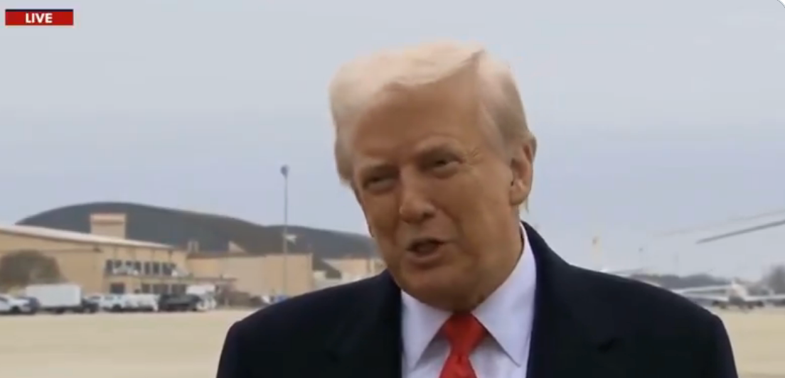 Trump in a suit speaks during a live broadcast at an airport location in the news
