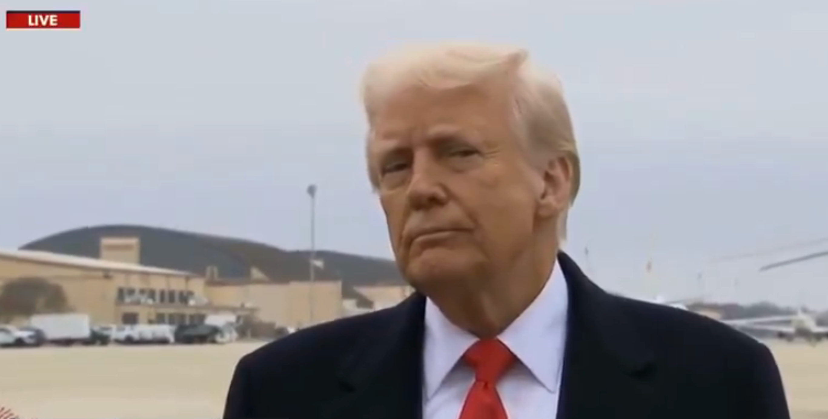 Trump in a suit and tie at an airport with a side-eye expression