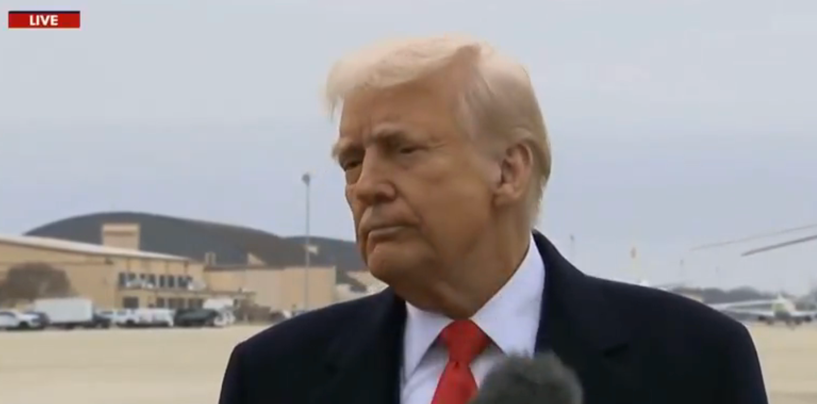 Trump at an airport, speaking to the media, staring at a reporter