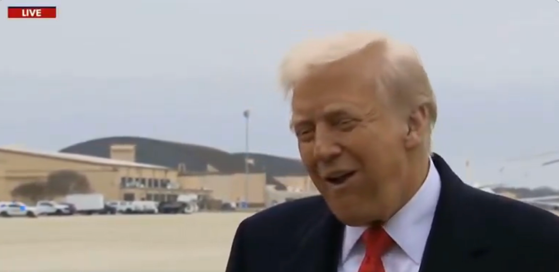 Trump speaking outdoors at an airfield smirking