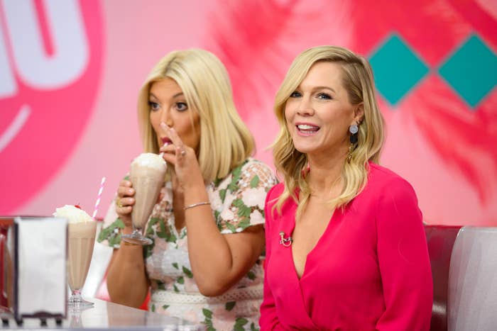 Tori Spelling sips a milkshake, wearing a floral dress while sitting next to a talk show host