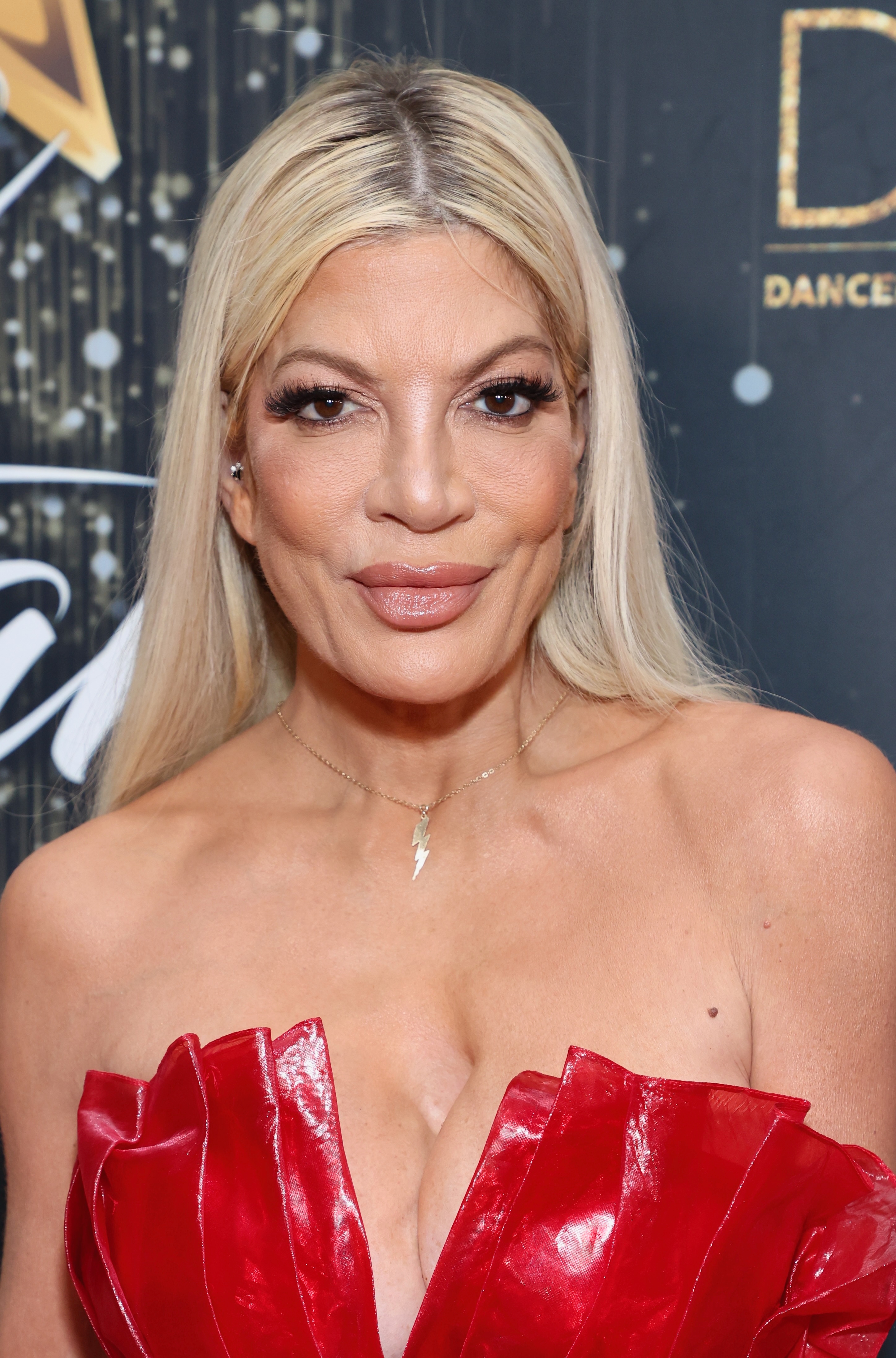 Tori Spelling on a red carpet wearing a strapless, ruffled outfit with her hair long and straight