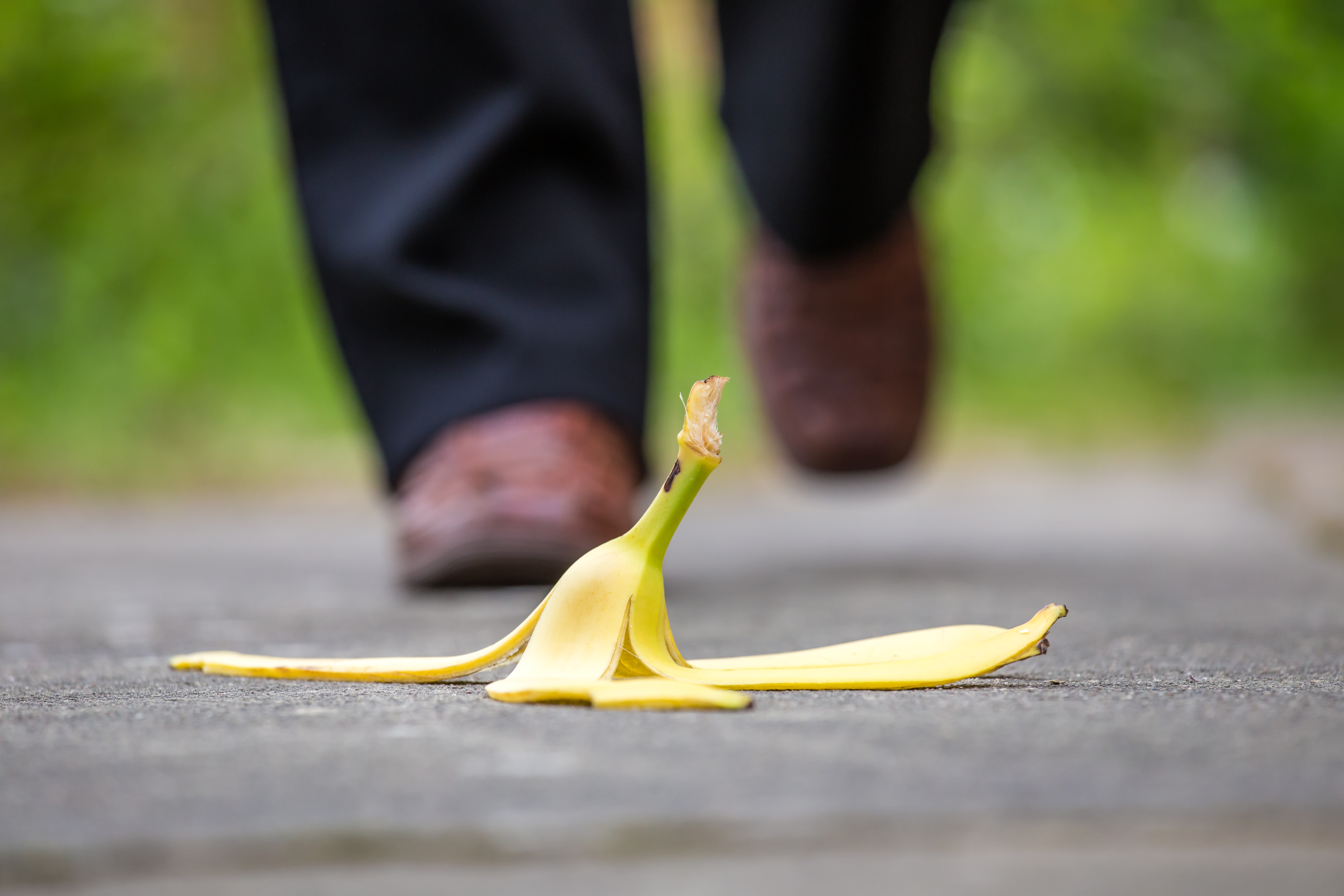 A person's feet approach a banana peel lying on the ground