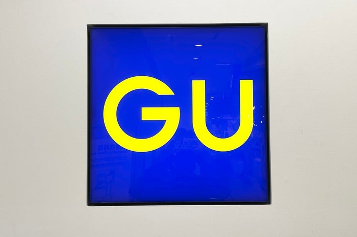 A bright store sign displays the large letters &ldquo;GU&rdquo; on a plain background