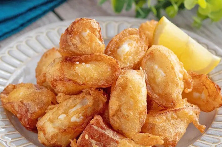 揚げた餃子の盛り合わせが皿に並べられ、レモンのくし切りが添えられています。背景に緑の葉があります。