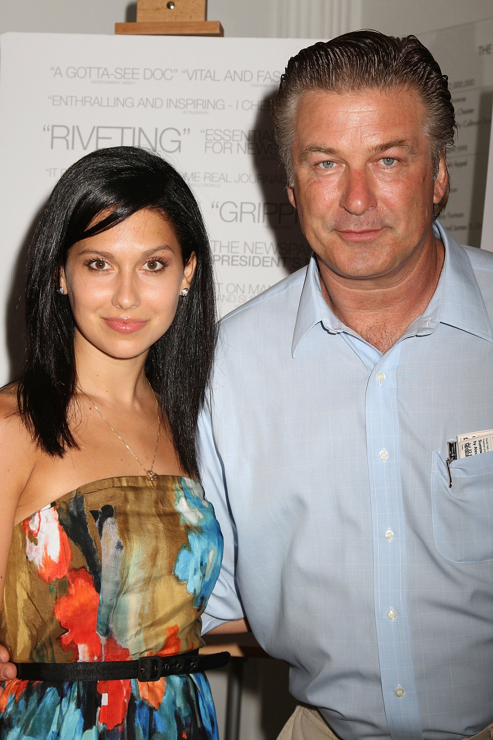 Two individuals pose together; the woman wears a strapless floral dress, and the man is in a casual button-up shirt