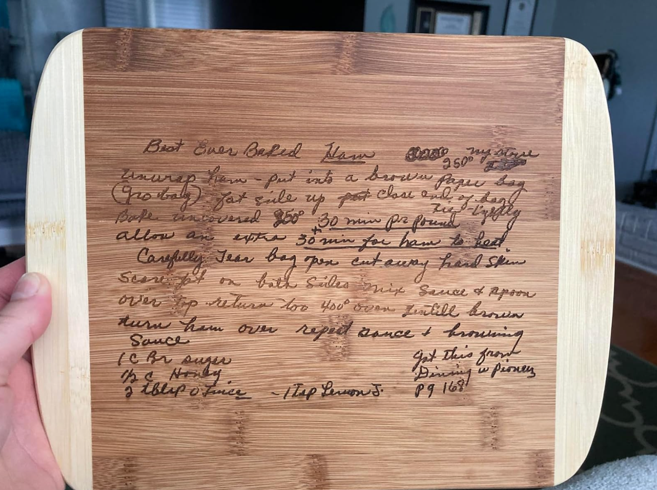 Hand holding bamboo cutting board with hand-written recipe for "Best Ever Baked Beans." Contains detailed cooking instructions and ingredients