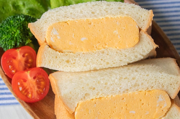 レタスとトマトが添えられた、厚焼き卵サンドイッチが木の板の上に置かれています。