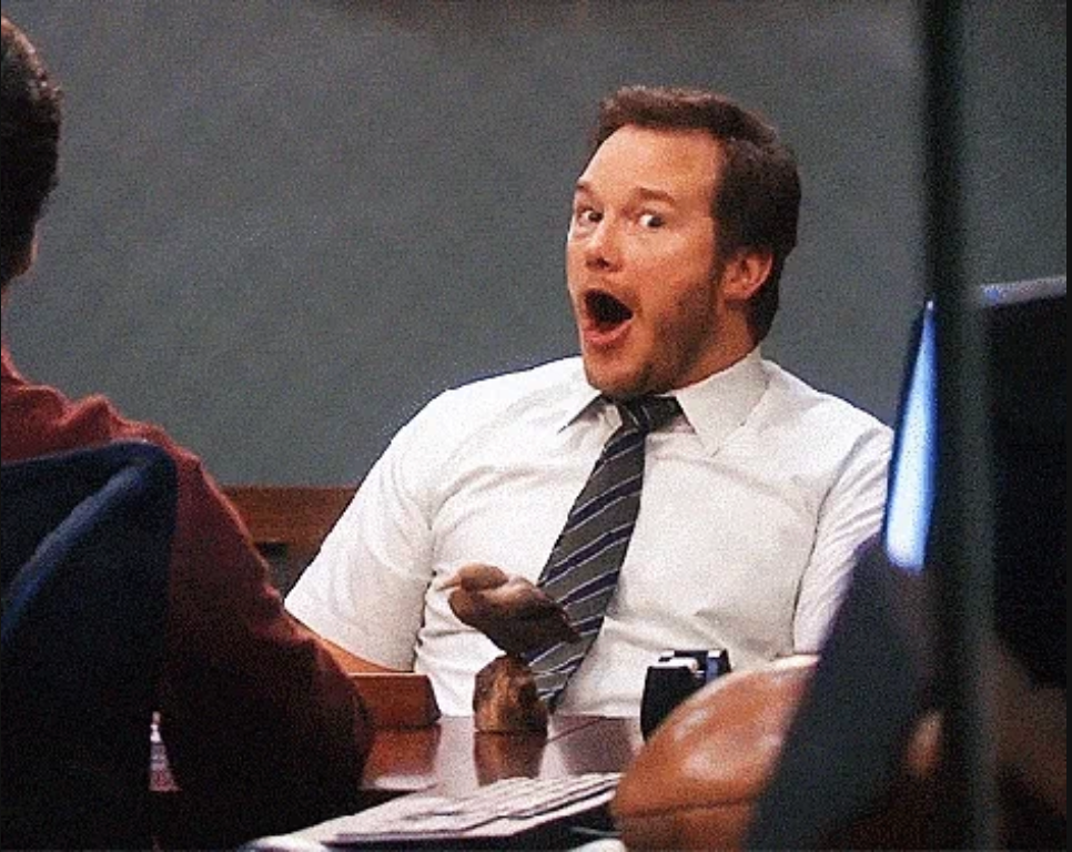 Person in an office setting, wearing a tie, looking surprised and amused
