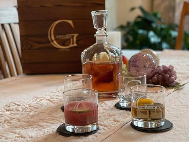 Whiskey decanter set on a table with personalized wooden box and four glasses containing fruit-infused drinks; perfect for enhancing home bar decor