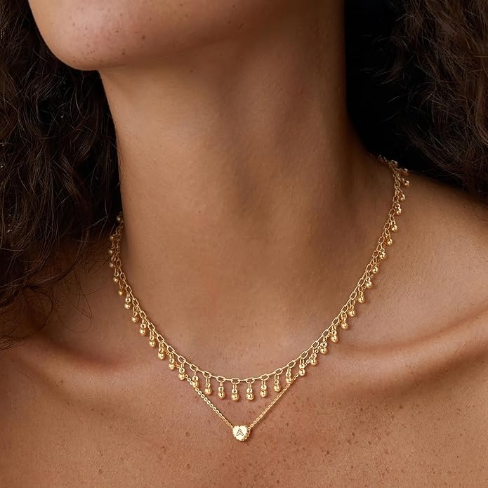 Person wearing layered gold necklaces with small dangling beads, creating an elegant and stylish look