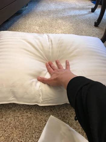 reviewer pressing into a plush pillow connected a carpeted floor, showcasing the pillow’s softness and comfort