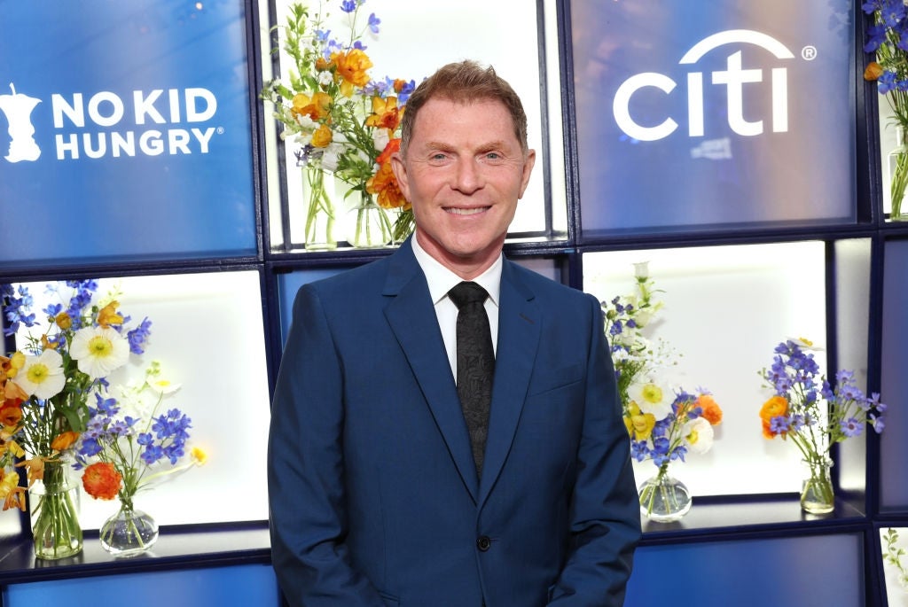 Person in a dark suit and tie at an event backdrop with floral arrangements and "No Kid Hungry" branding