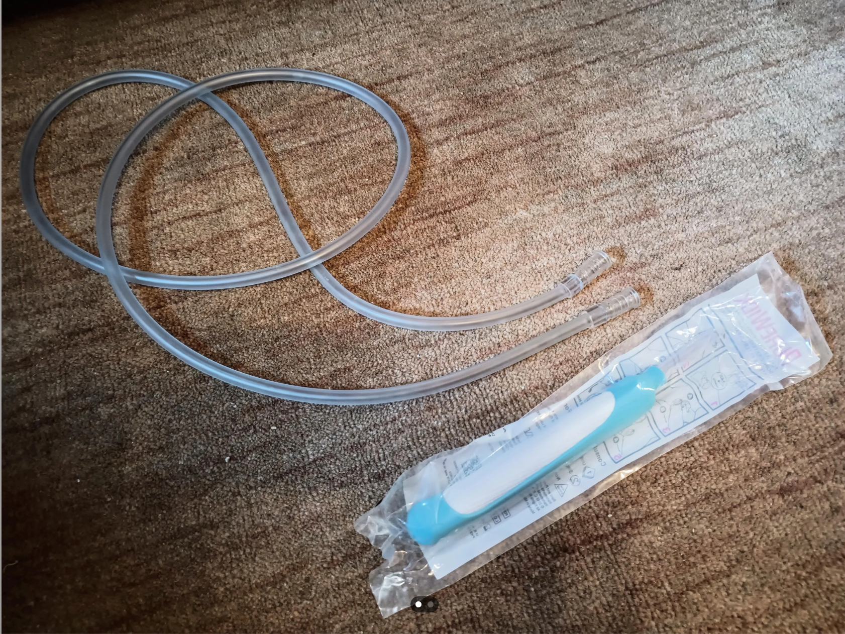 A nasal aspirator with a long tube next to a plastic handle, resting on a carpeted surface