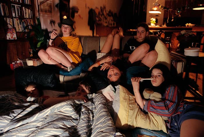Group of people lounging in a cozy living room with pillows and blankets, watching TV together