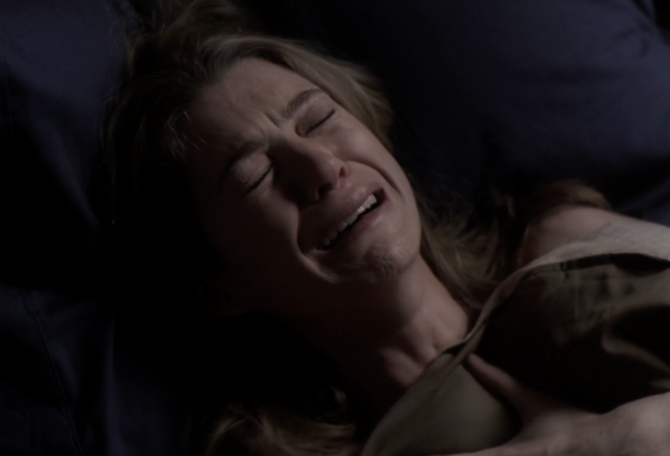 Ellen Pompeo lying in bed, visibly upset, clutching the blanket with her eyes closed