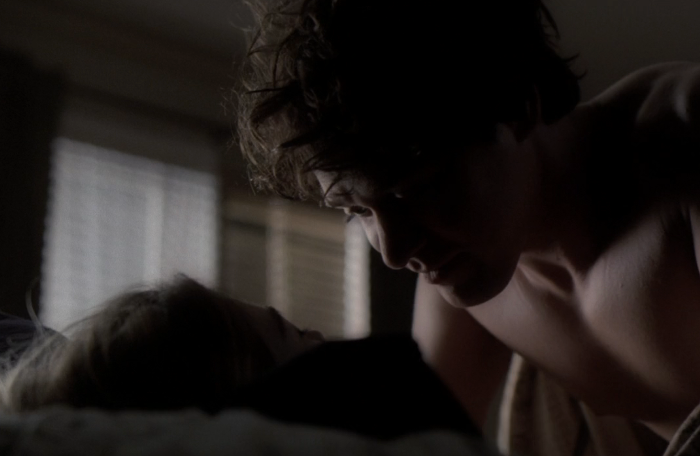 T.R. Knight in a scene from "Grey's Anatomy," leaning over Ellen Pompeo's Meredith Grey in bed, in a dimly lit room