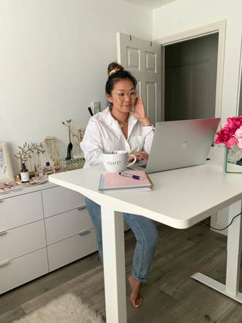 another reviewer successful a casual blouse and jeans moving astatine a lasting table with a laptop, notebook, and mug, successful a stylish location bureau setting