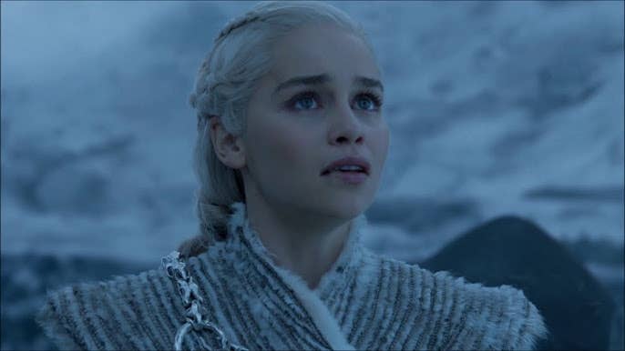 A character with braided hair and a fur outfit looks up, appearing determined in a snowy landscape, from a scene in TV series or movie