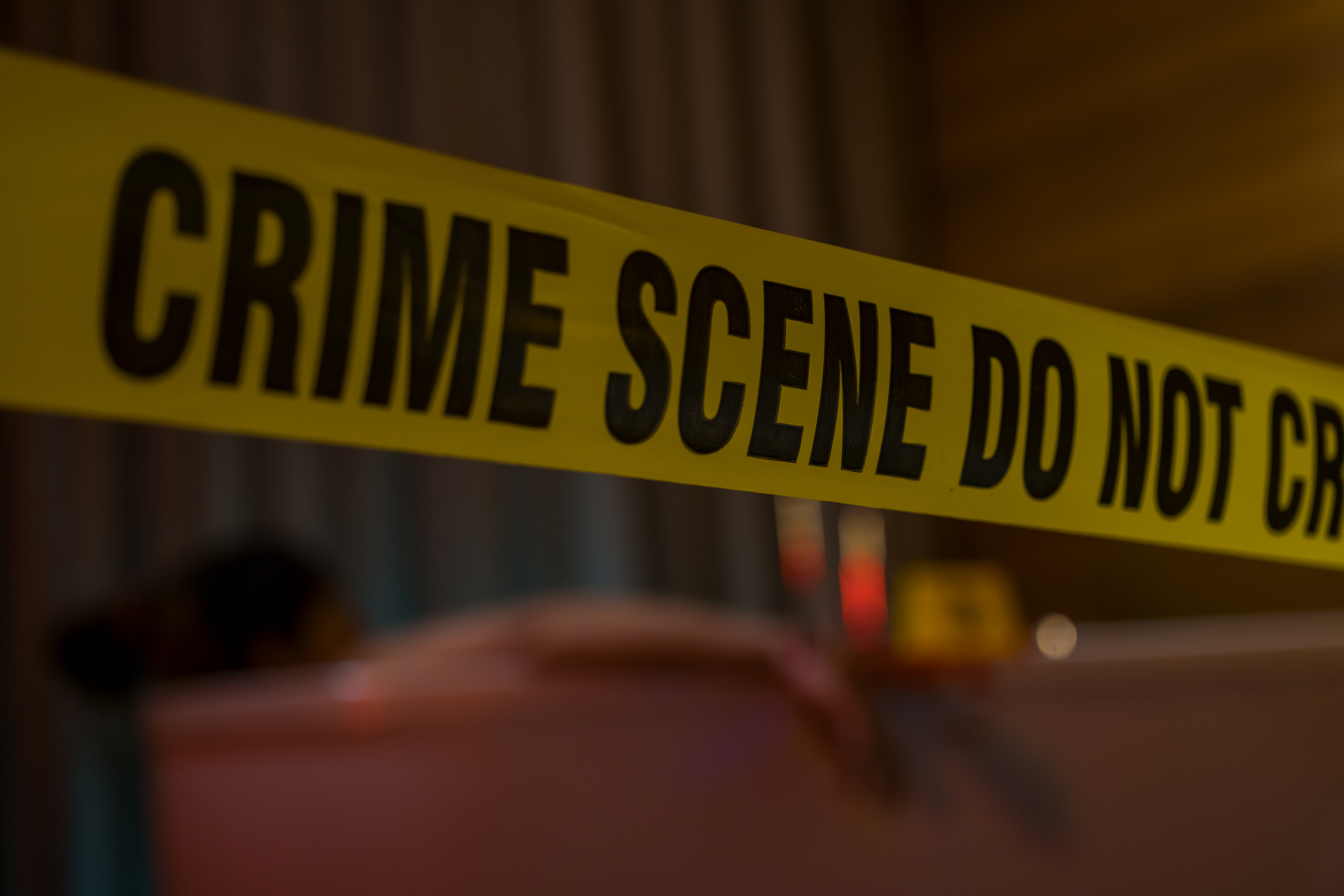 Crime scene tape with "Crime Scene Do Not Cross" text in focus, blurred background suggestive of an investigation setting