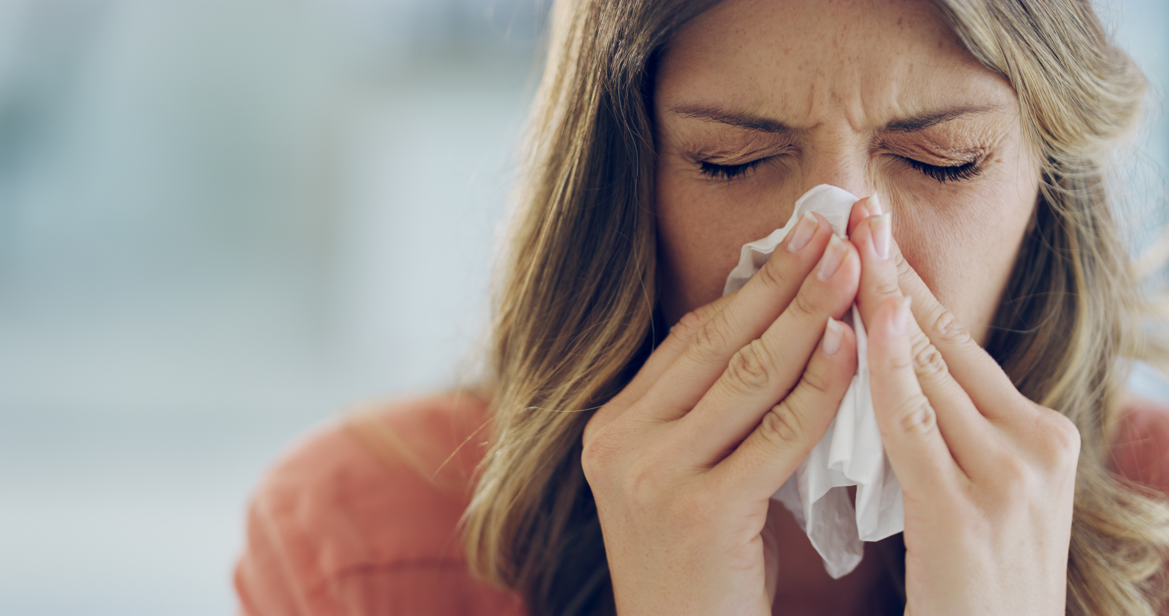 Woman sneezing into a tissue, eyes closed