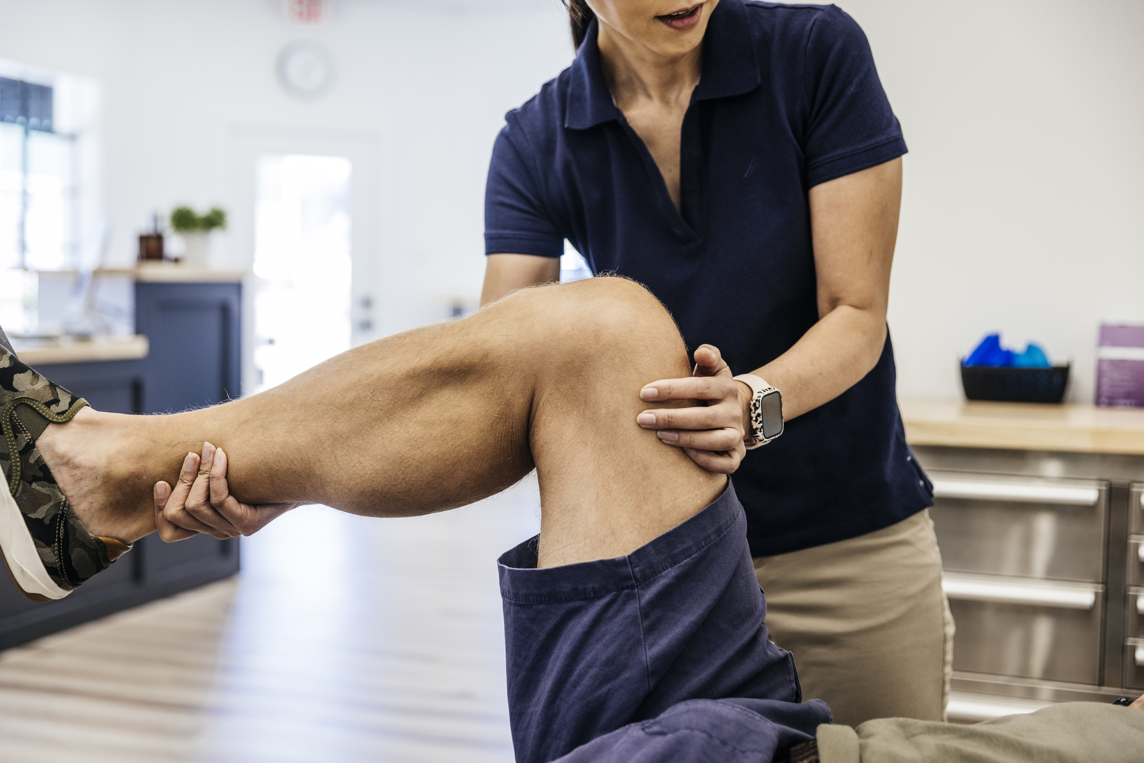 A physical therapist assists a person with a knee exercise in a therapy room