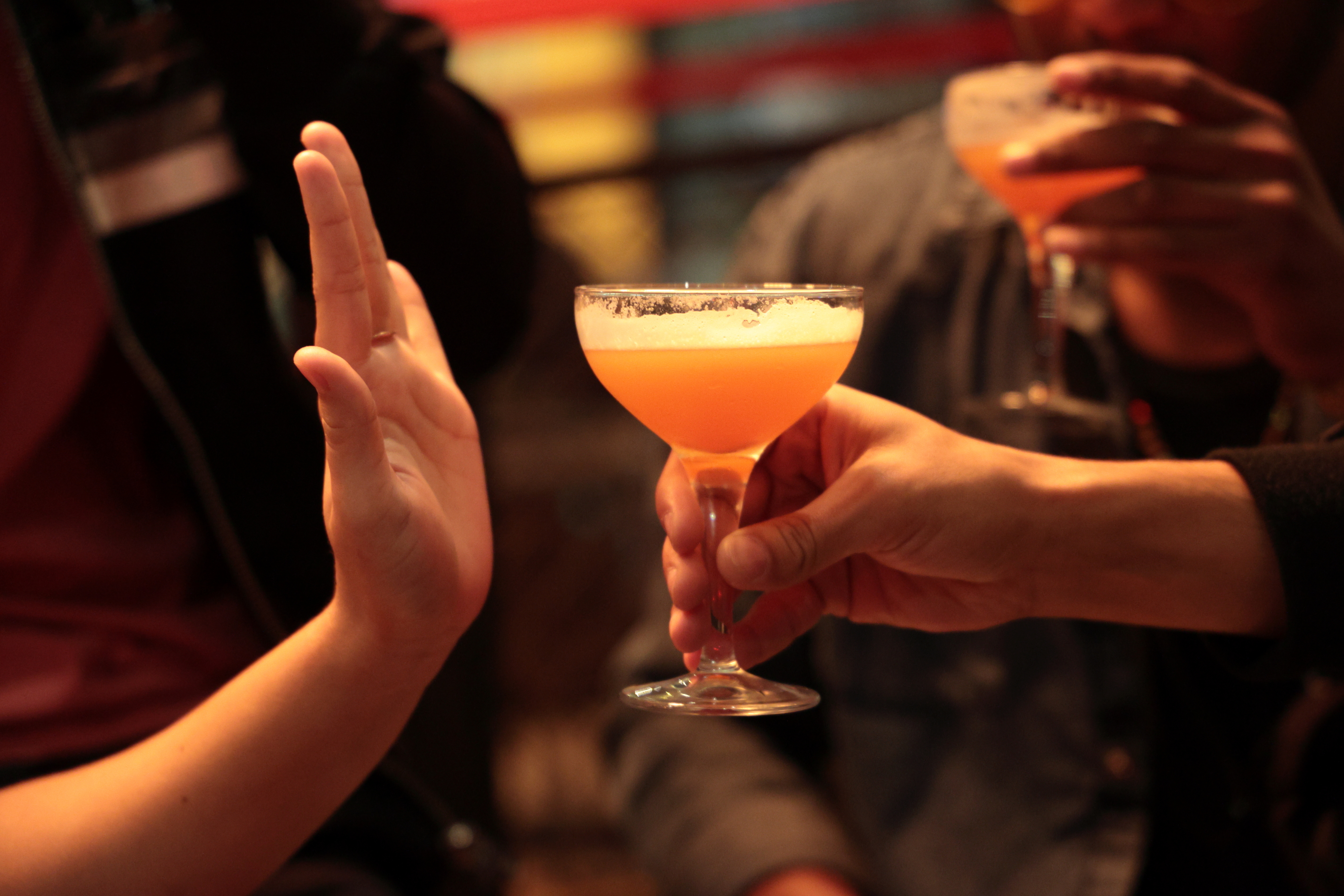 Person refusing a cocktail, hand up in a stop gesture, while another offers a drink. Social interaction scene
