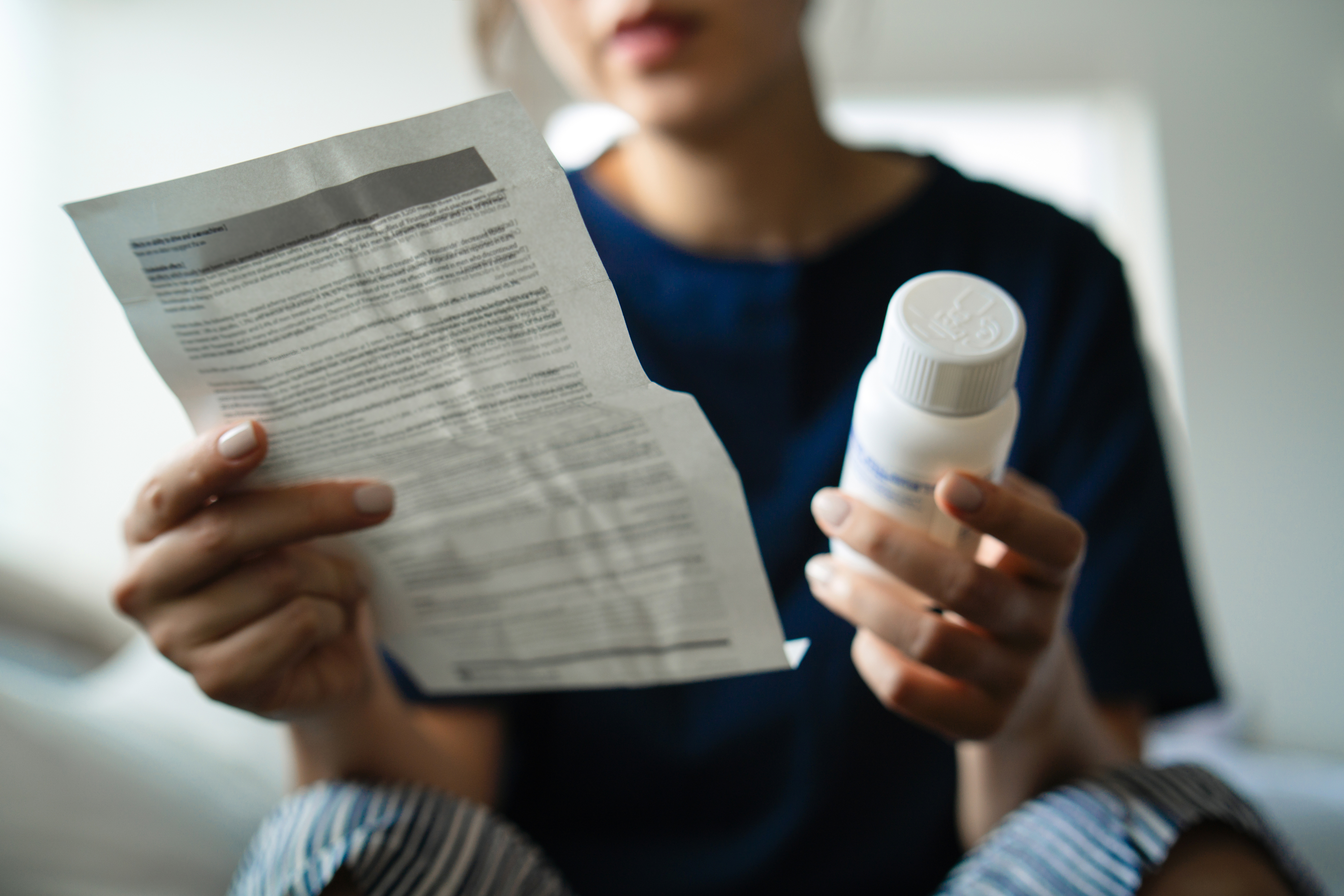 Person reading a medication leaflet while holding a prescription bottle, suggesting focus on instructions or dosage